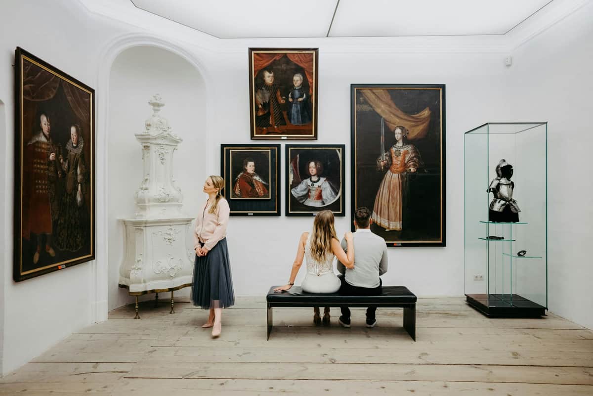 Forchtenstein Castle: Entry Ticket A couple sits on a bench viewing portraits in an art gallery while a woman stands nearby, observing the surroundings.