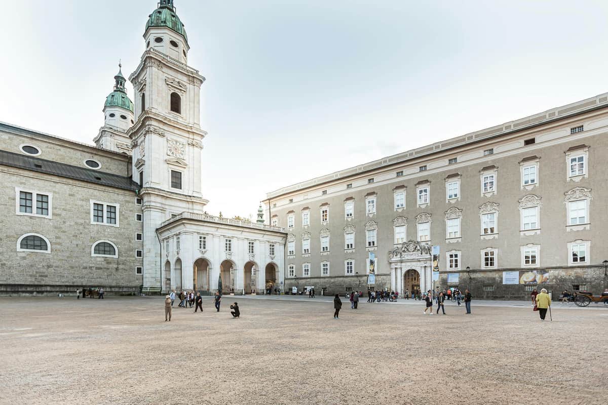 DomQuartier Salzburg: Entry Ticket People walk and gather in a large, open square surrounded by historic buildings, including a church with tall towers.