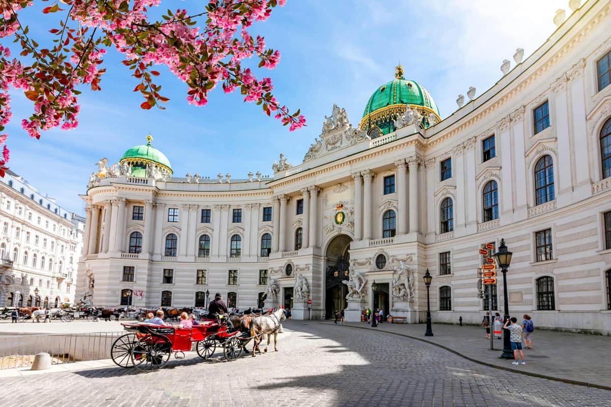 Sisi Museum, Hofburg Palace & Vienna Gardens: Skip The Line + Guided Tour Ornate historic building with green domes, horse-drawn carriage in foreground, and blooming cherry blossom branch above.