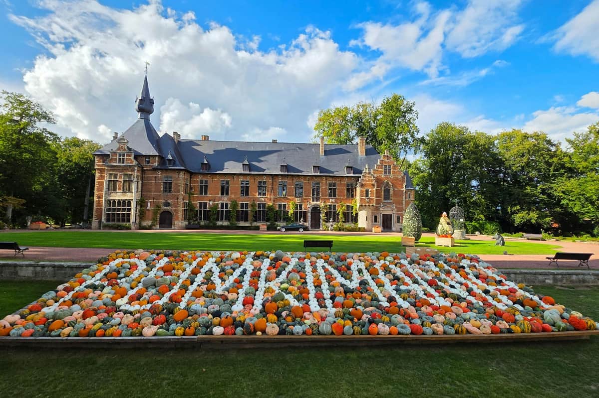 Groot-Bijgaarden Castle: Pumpkimania 2025 A historic building with a sloped roof behind a colorful pumpkin display spelling "PUMPKINS," under a partly cloudy sky.