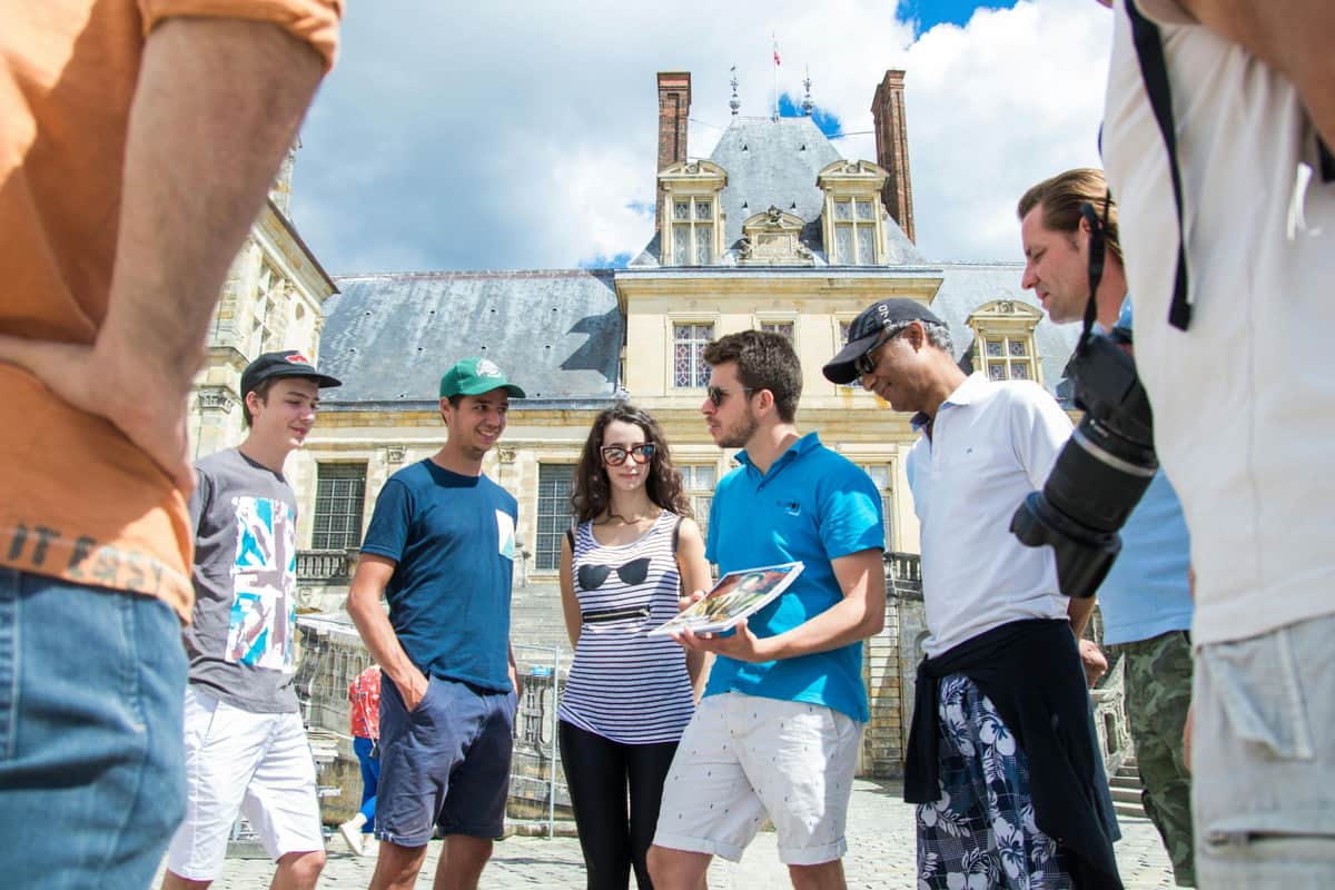 A group of people standing outdoors near a historic building with a cloudy sky in the background.