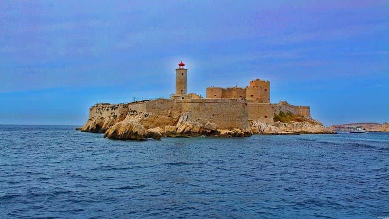 Stone fortress with a lighthouse on a rocky island, surrounded by blue ocean under a clear sky.