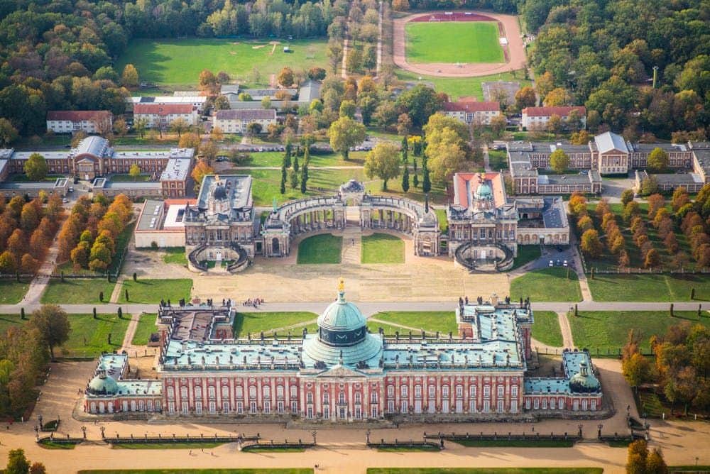 Potsdam & Sanssouci Palace: Guided Tour from Berlin Aerial view of a large baroque palace with a green dome, courtyards, and surrounding formal gardens and buildings.