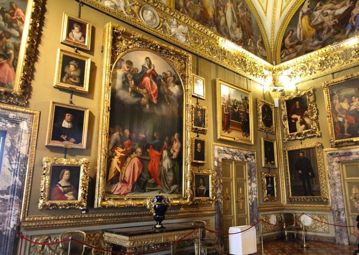 Palazzo Pitti & Palatine Gallery: Entry Ticket + Guided Tour A wall adorned with numerous framed classical paintings, centered by a large ornate painting, in a richly decorated room.