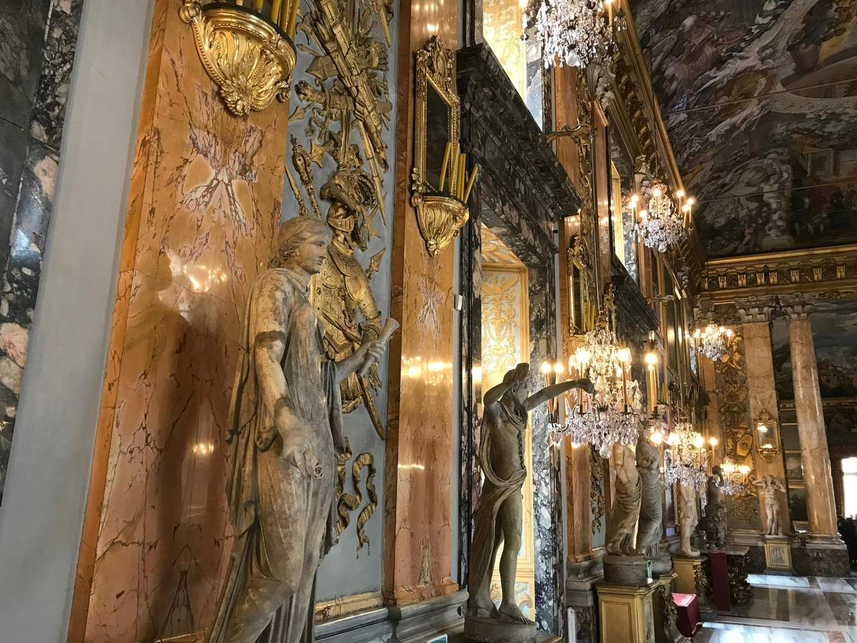 Colonna Gallery Luxurious hall with marble columns, ornate statues, crystal chandeliers, and gold detailing on the walls and ceiling.