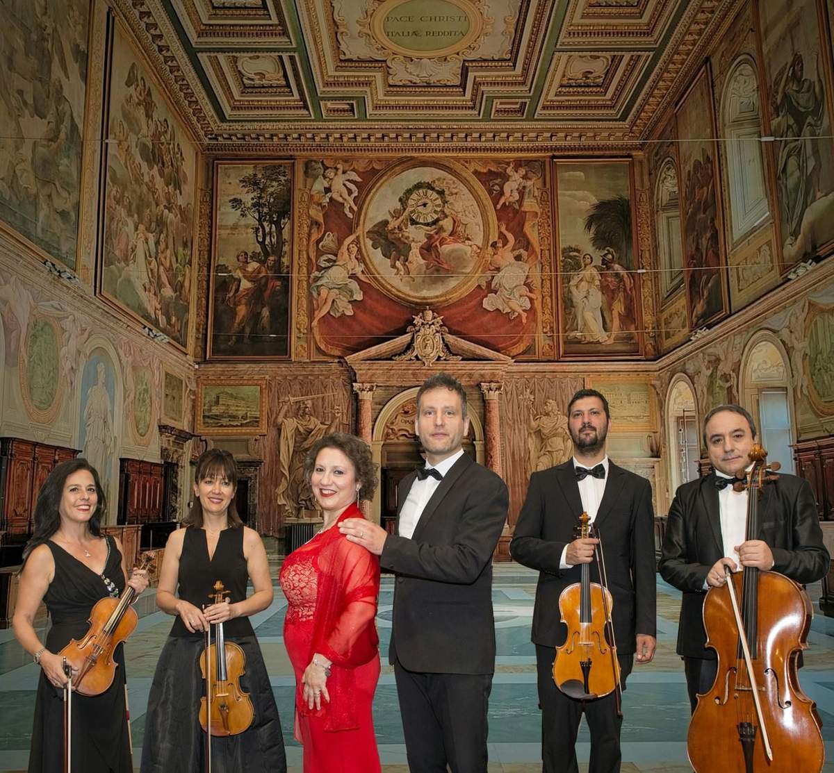 A group of six musicians dressed formally, holding string instruments, posing in an ornate, fresco-decorated hall.
