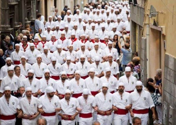 Viterbo Pass A large group of people in matching white outfits with red sashes and head coverings walking down a narrow, crowded street.