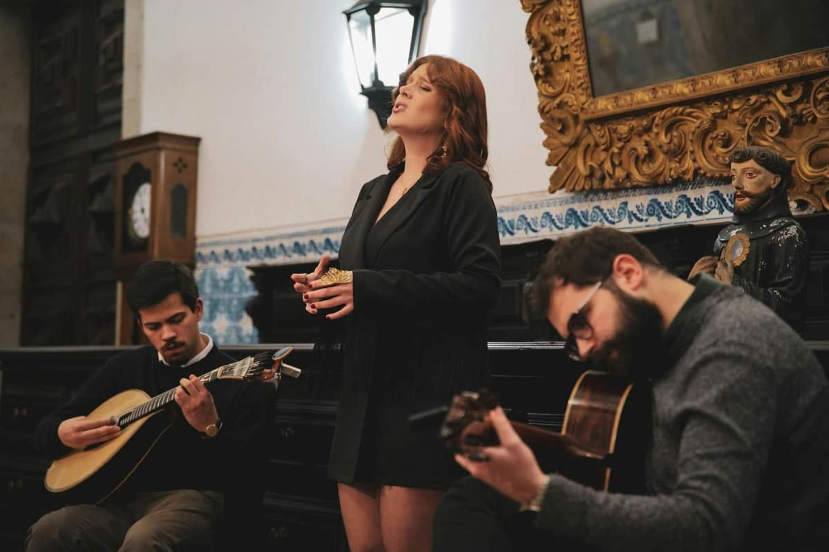 Porto: Self-Guided Monastery Tour + Fado Show + Drinks A woman sings while two men play string instruments in an indoor setting with decorative walls and furniture.
