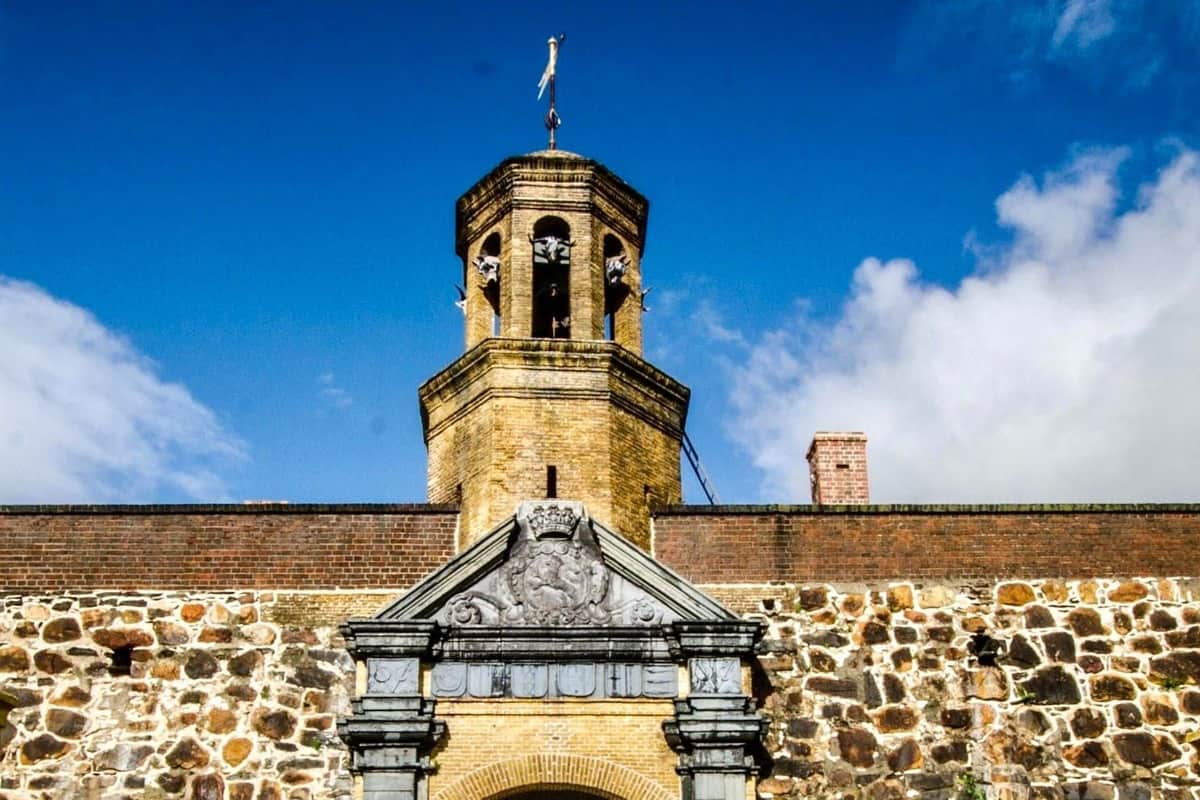 Castle of Good Hope: Guided Tour Stone building with an arched entrance, ornate carvings, and a bell tower against a blue sky with clouds.