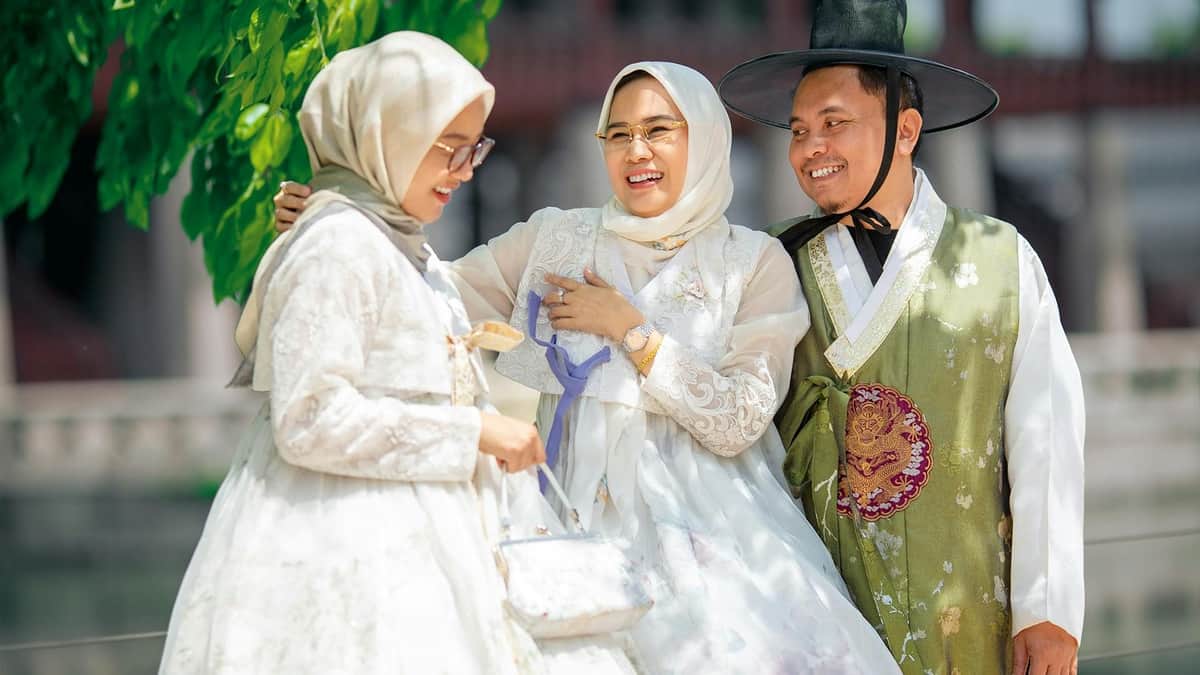 Daehan Hanbok: Gyeongbokgung Hanbok Rental & Photoshoot Experience + Premium Hanbok Rental Three people wearing traditional clothing, smiling and interacting outdoors in a bright, sunny setting.