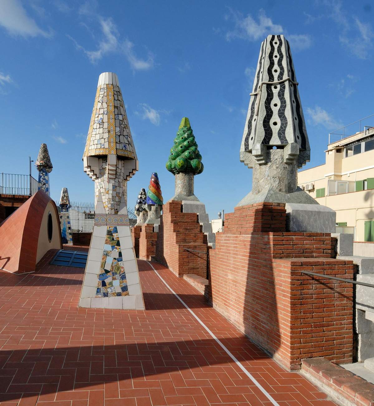 Architectural rooftop featuring colorful, mosaic-covered sculptural chimneys and brick structures under a clear blue sky.