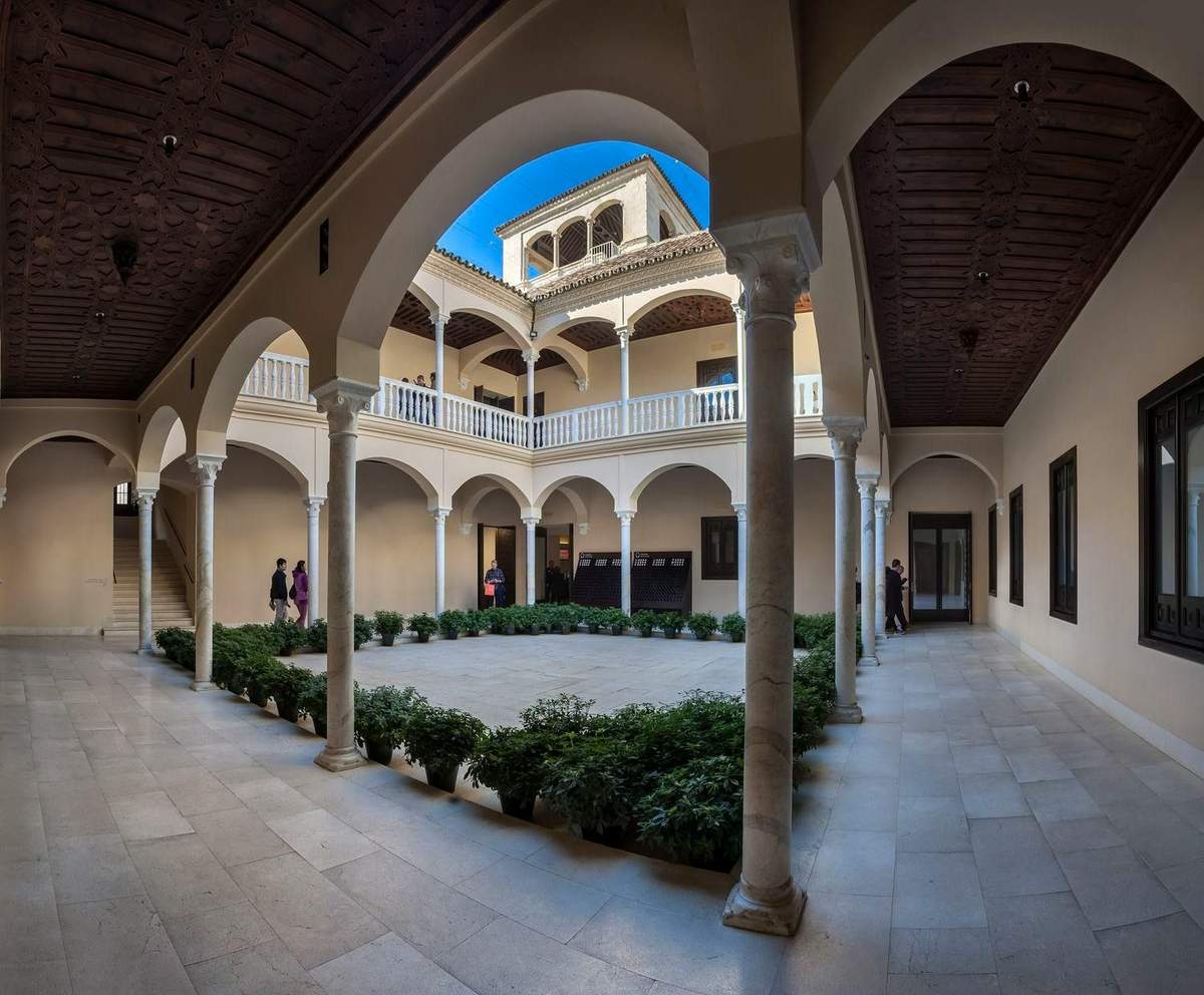 Museo Picasso Málaga: Entry + Audio Guide Interior courtyard with arched columns and upper balcony. A few people walk along the perimeter. Plants line the central area.