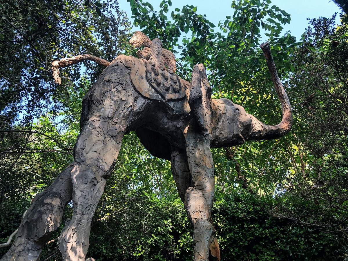 A mud sculpture of an elephant with a person riding it, surrounded by dense green foliage and trees.