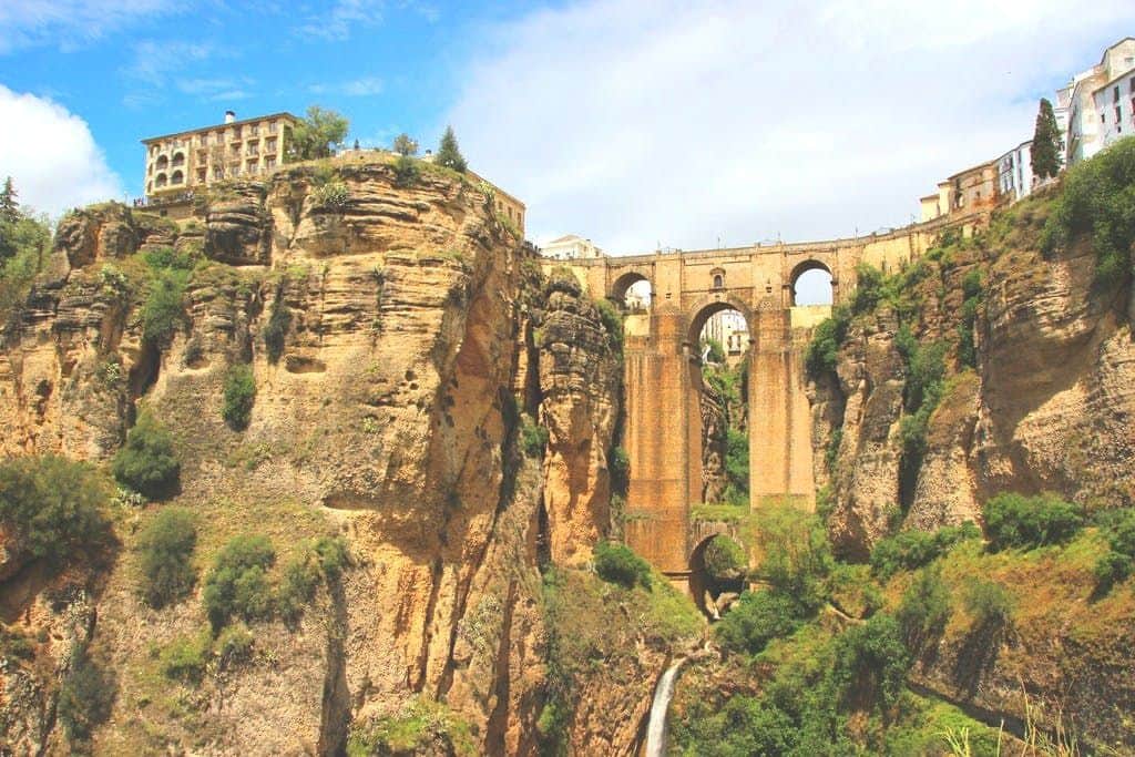 Un alto ponte di pietra attraversa una profonda gola, con edifici in cima alle scogliere e una cascata che scorre sotto.
