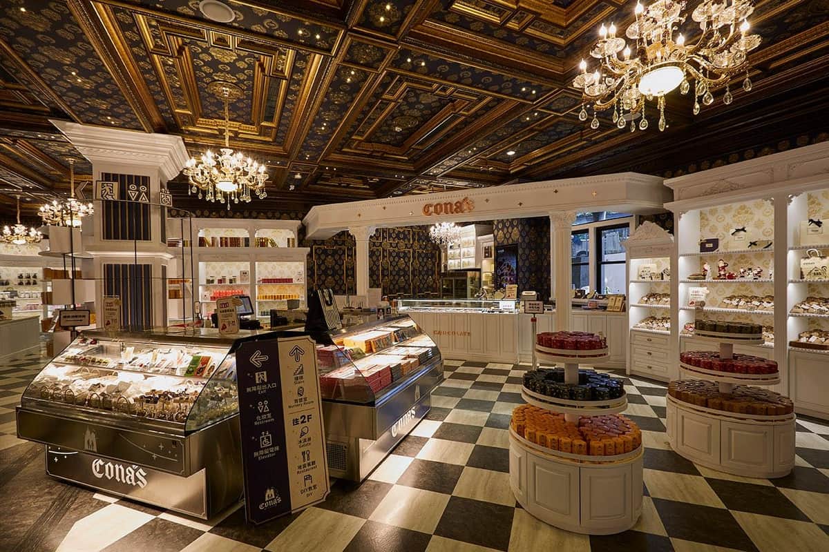 A stylish confectionery store with elegant lighting, ornate ceiling, and displays of colorful sweets on counters and shelves.