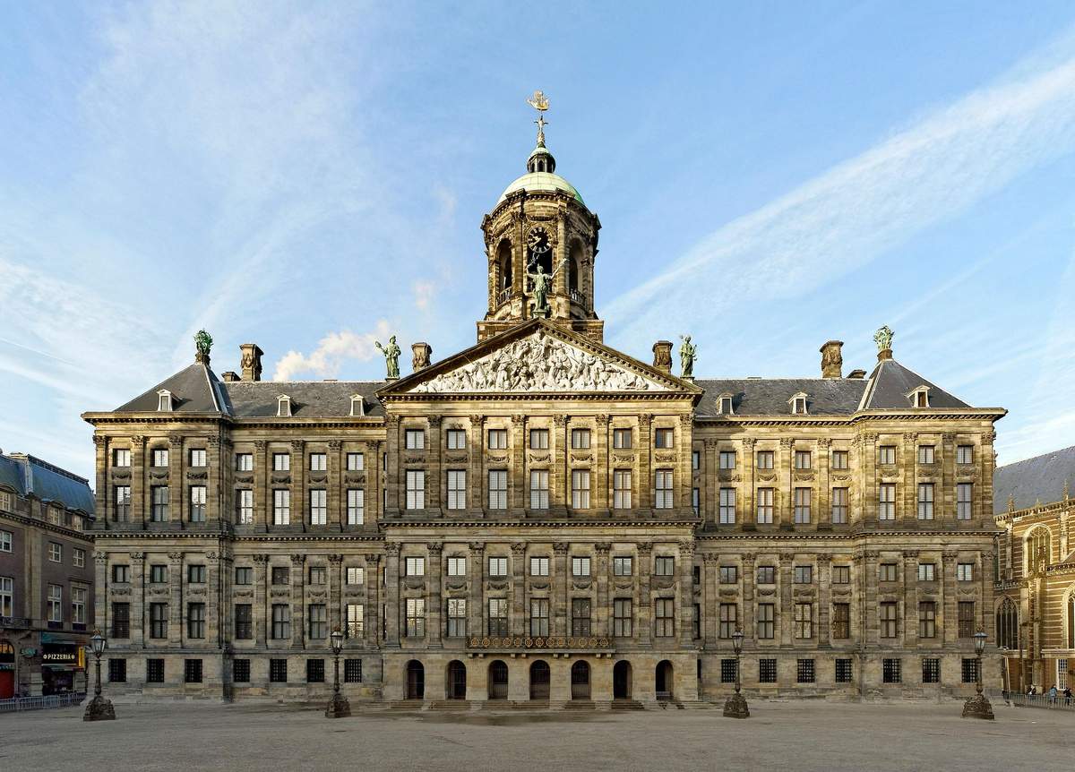 A large, historic building with symmetrical architecture, many windows, a central tower with a clock, and a clear blue sky.