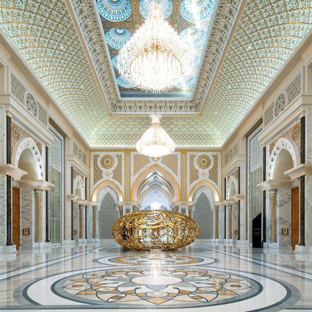 Qasr Al Watan Palace: Entry Ticket A grand hall with ornate arches, chandeliers, intricate ceiling designs, and a large gold sculpture in the center.