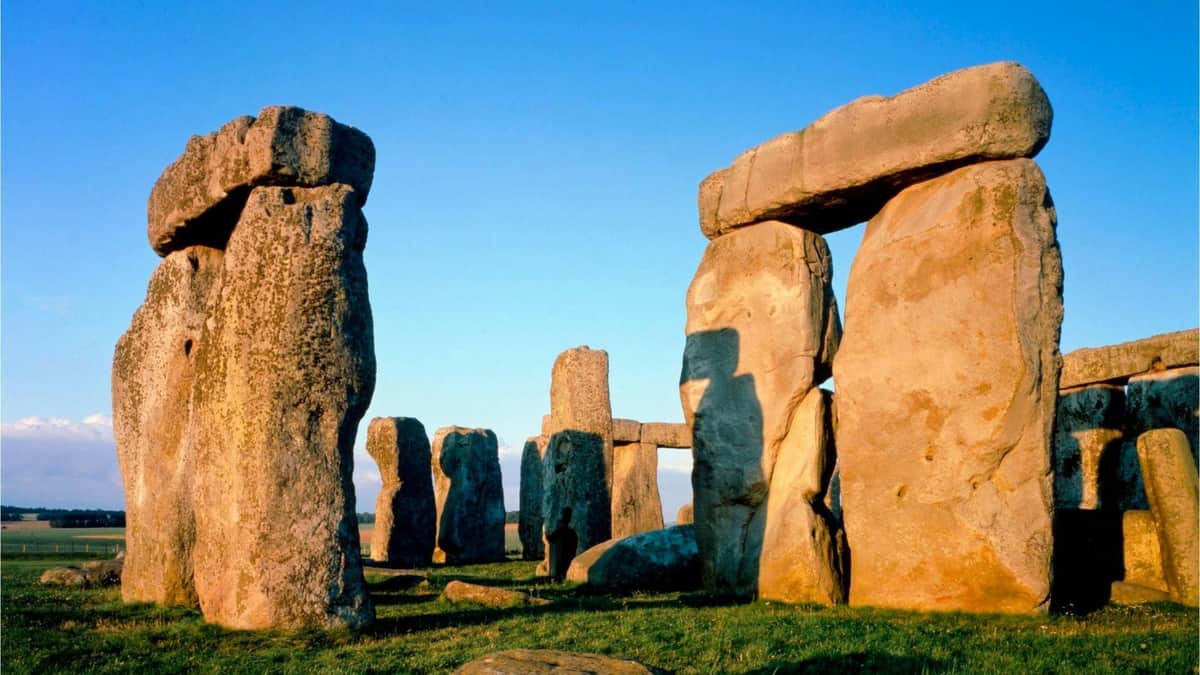 Stonehenge, Windsor Castle & Oxford: Day Trip from London Large stone monoliths forming a circle on grass, under a clear blue sky, likely part of an ancient structure.