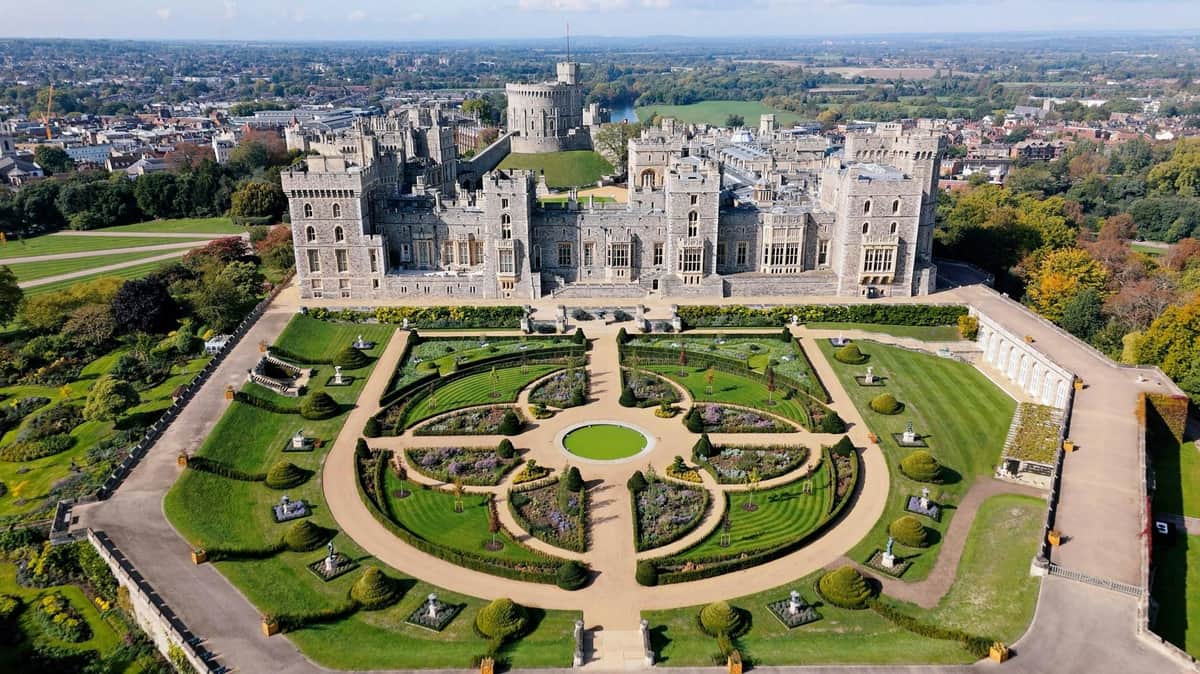 Windsor Castle: Entry Ticket Aerial view of a large castle with intricate gardens featuring symmetrical pathways and greenery in the foreground.