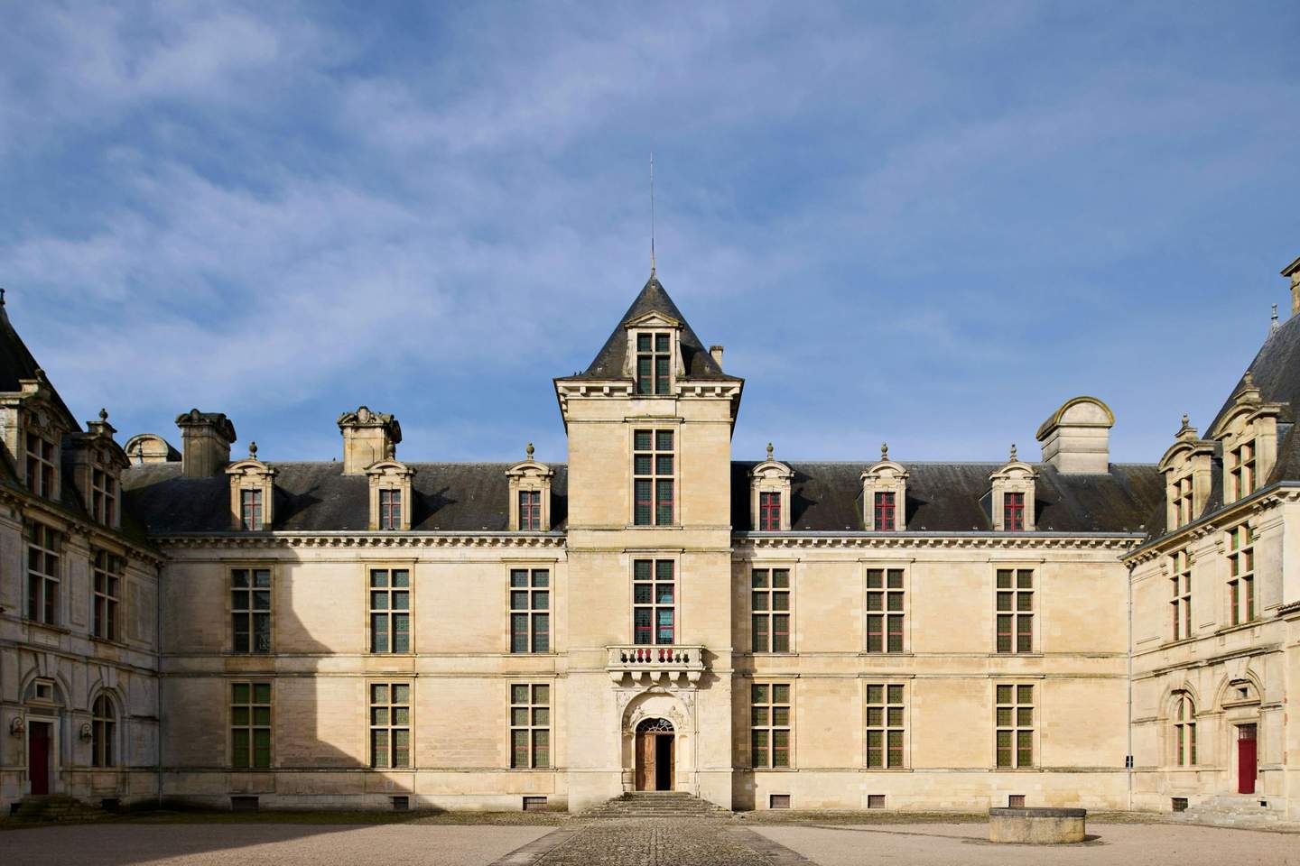 Historic chateau with symmetrical facades, tall windows, and a central tower, under a clear blue sky.