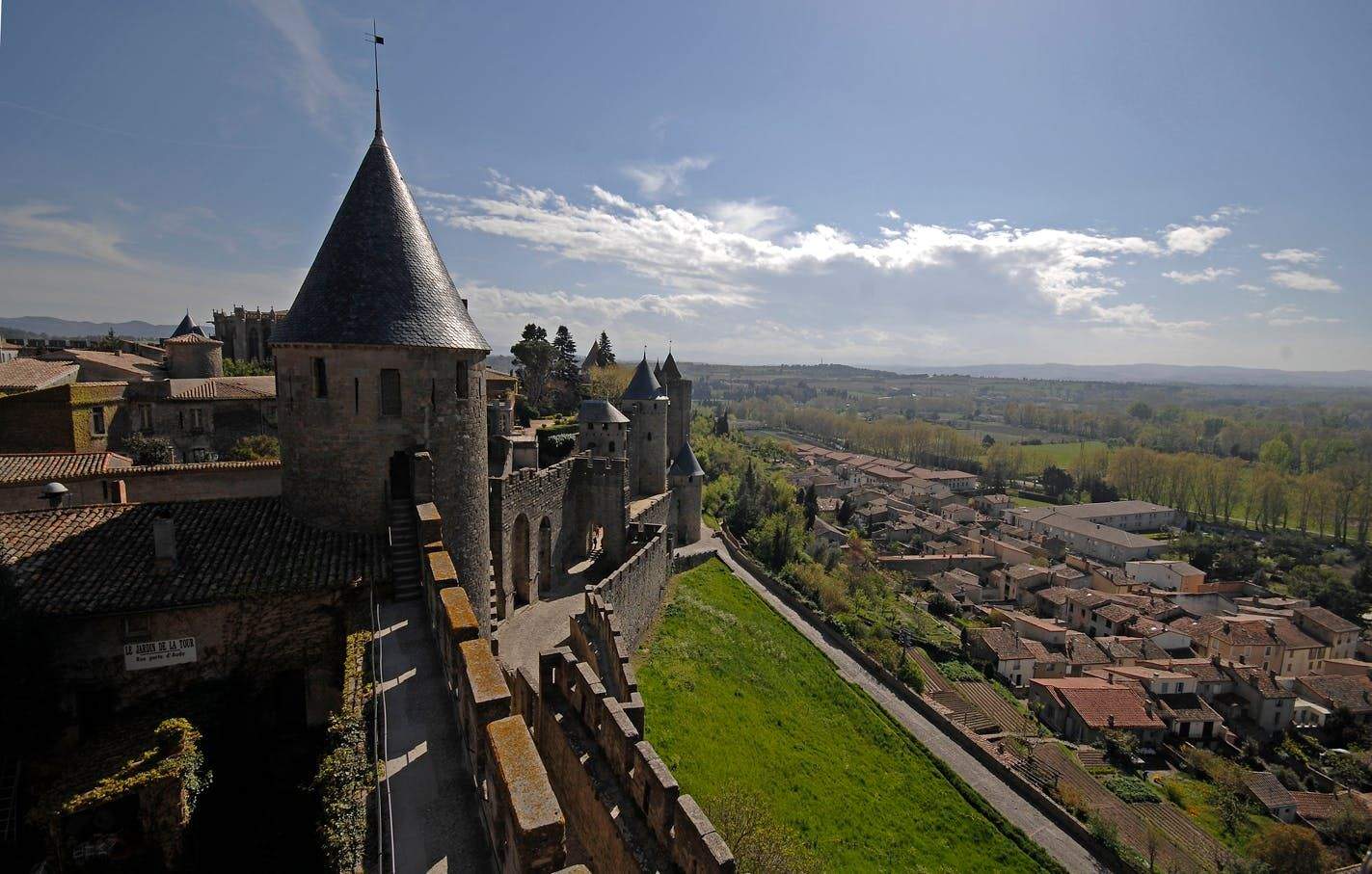 Cité de Carcassonne A historic stone castle with conical towers overlooks a town with red-tiled roofs and a green landscape in the distance.