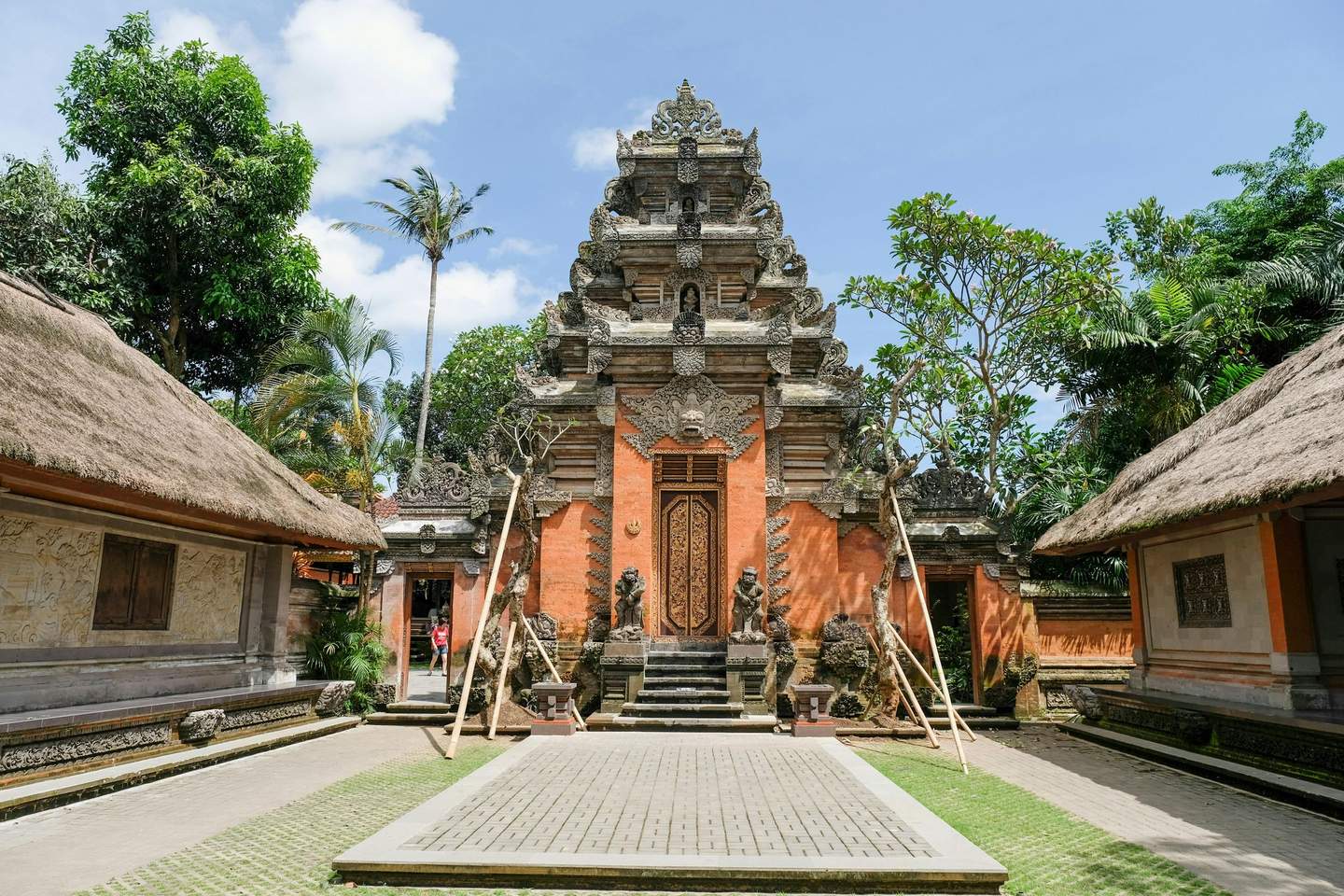 Ubud Palace Ornate temple entrance with intricately carved details, flanked by lush greenery and traditional thatched-roof structures.
