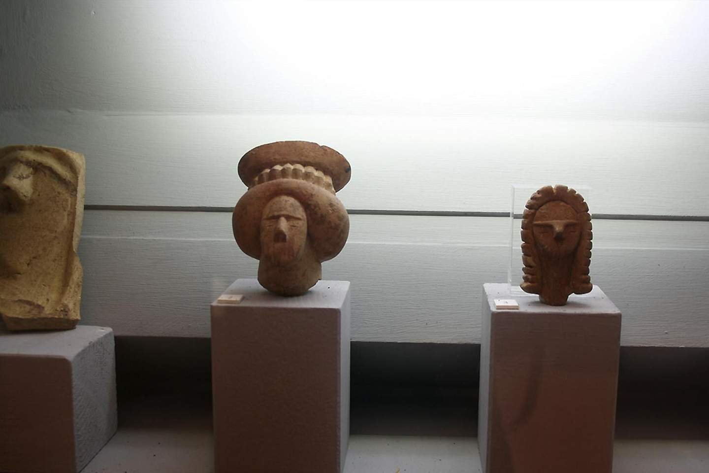 Three ancient stone sculptures displayed on individual pedestals under soft lighting.