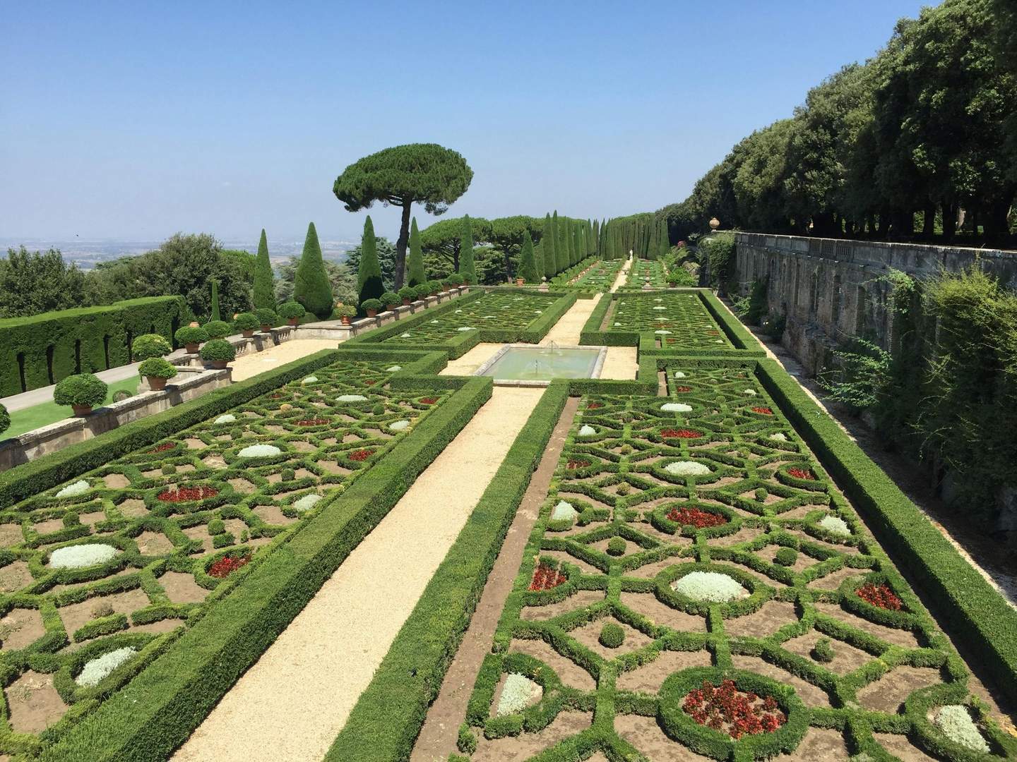 Papstpalast & Gärten von Castel Gandolfo Formeller Garten mit verschlungenen Hecken, geometrischen Mustern und einem zentralen Kiesweg, der von beschnittenen Bäumen und Sträuchern gesäumt wird.
