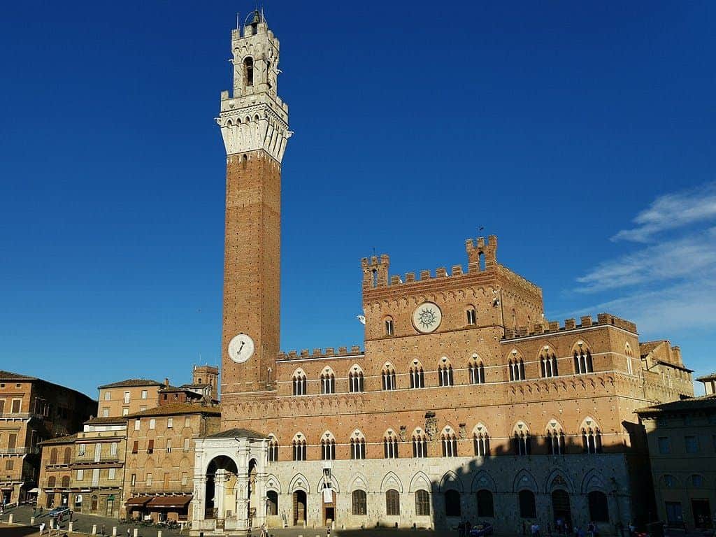 Historic brick building with a tall clock tower and battlements against a clear blue sky.