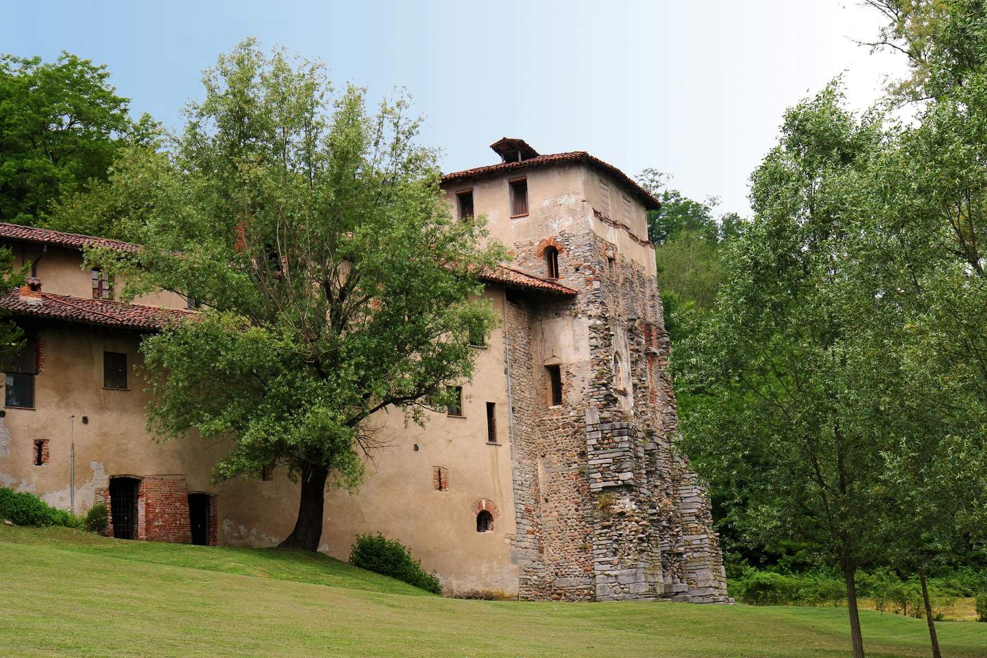 Torba Monastery Ancient stone building with a tiled roof, surrounded by trees and greenery on a clear day.