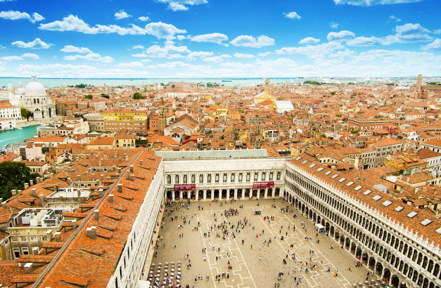 St Mark's Square Aerial view of Venice, showing a large open square surrounded by buildings with red rooftops and a canal with domed structures.