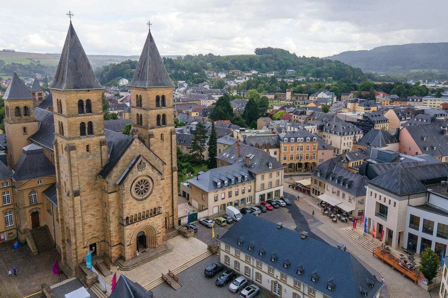 Catedral de Notre-Dame de Luxemburgo Vista aérea de un pueblecito con una catedral que destaca, los edificios que la rodean y un paisaje montañoso al fondo.