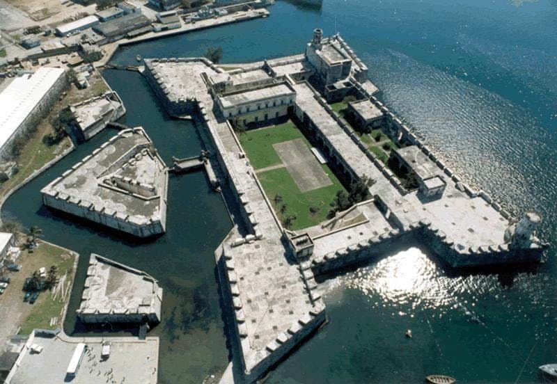 Aerial view of a large, star-shaped historic fortress surrounded by water, with a green courtyard and several buildings.