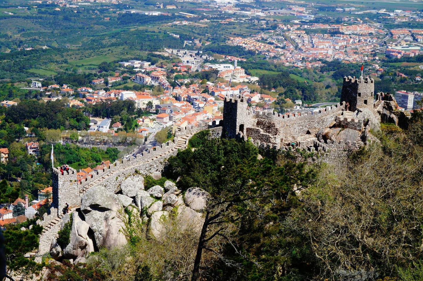 Castelo dos Mouros Sintra Ancient stone castle walls on a hilltop with a view of a town and green landscape below.