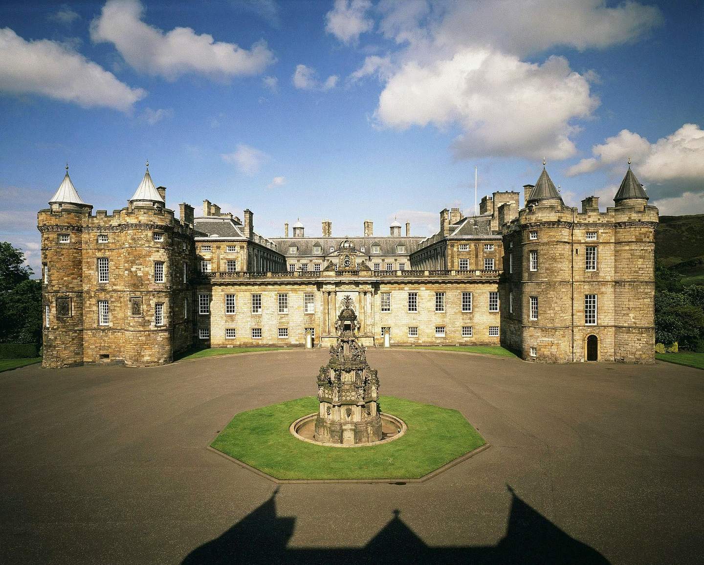 Historic stone castle with cylindrical towers, symmetrical structure, and a central courtyard featuring an ornate fountain.